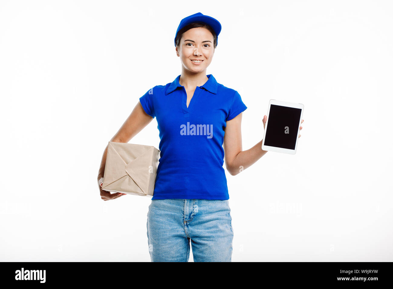 Post office Lavoratore che indossa uniformi e jeans pone la fotocamera tenendo un pacco e un tablet. Sorride come se lei guarda a qualcuno. Foto Stock