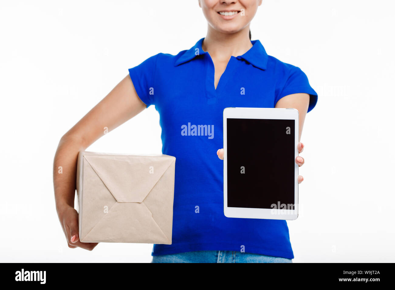 Close up di un ufficio postale lavoratore nell'uniforme di fronte a sua schermata compressa verso la telecamera e tenendo un grosso pacco di spedizione nella sua altra mano. Foto Stock