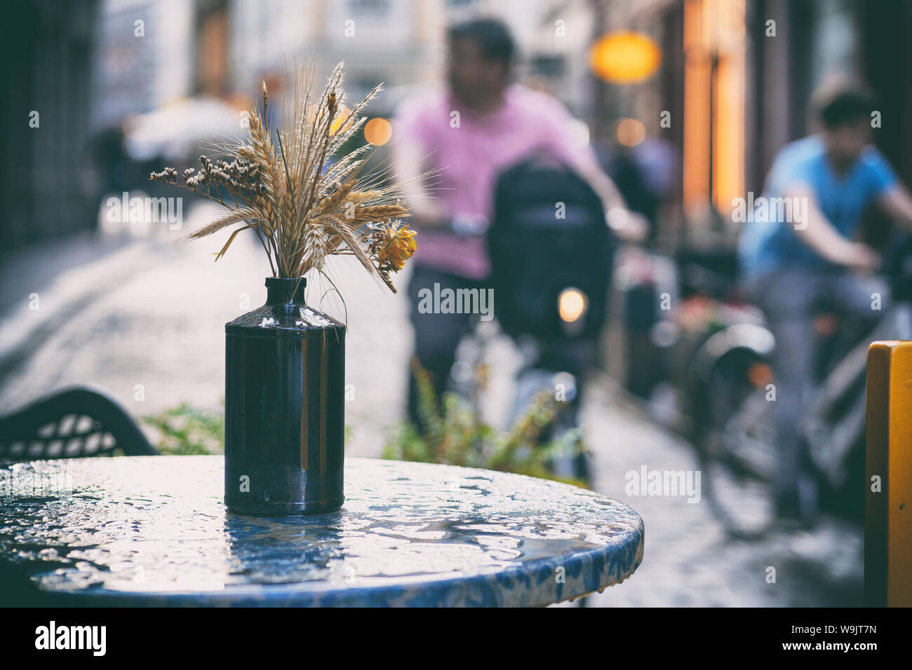 Un mazzo di fiori sul tavolo in una caffetteria estiva con gocce sul tavolo contro lo sfondo di turisti in bicicletta nella città vecchia Foto Stock