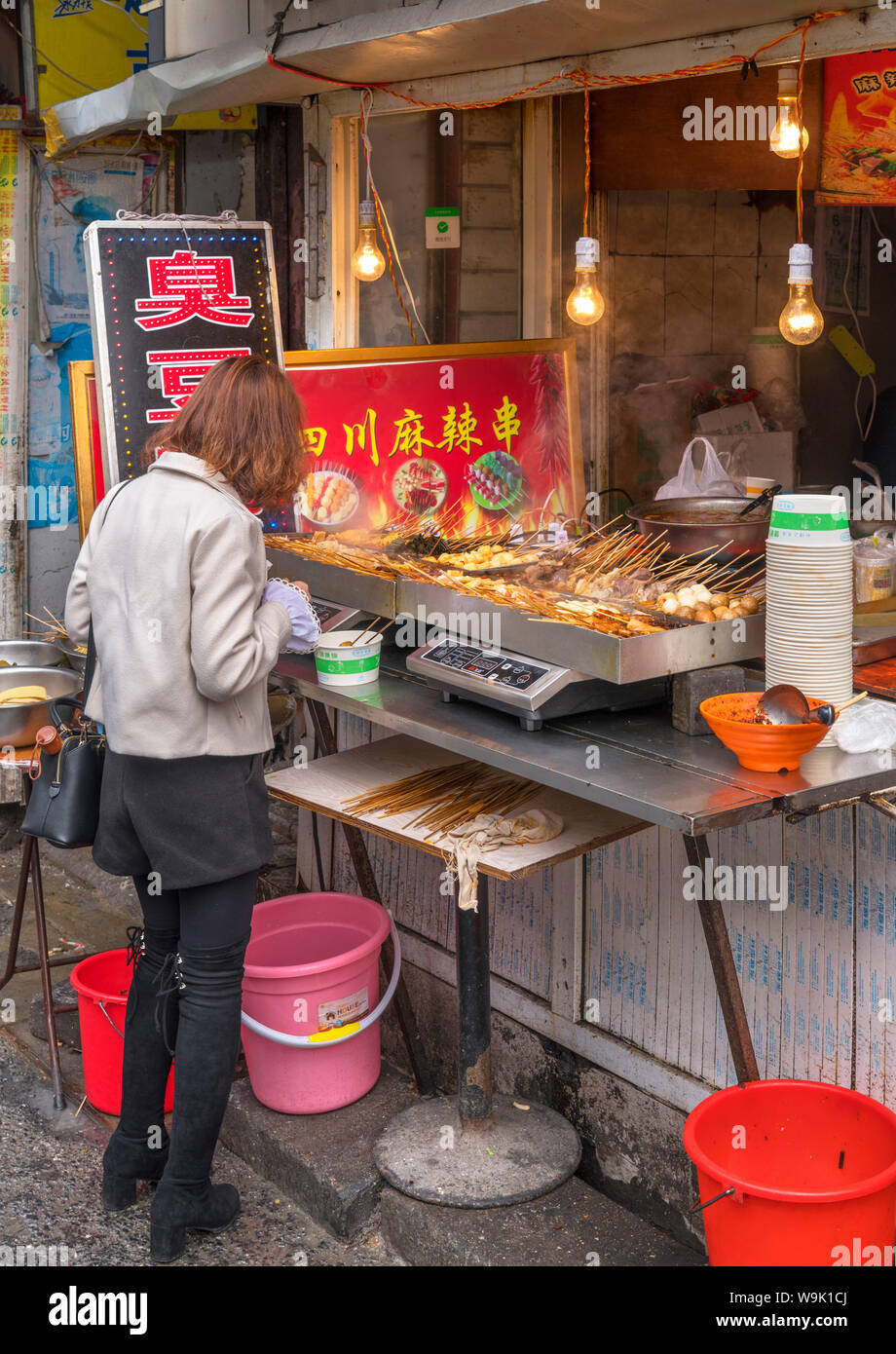 Shanghai street food. Giovane donna comprare cibo a un cibo tradizionale stallo nella Città Vecchia, Shanghai, Cina Foto Stock