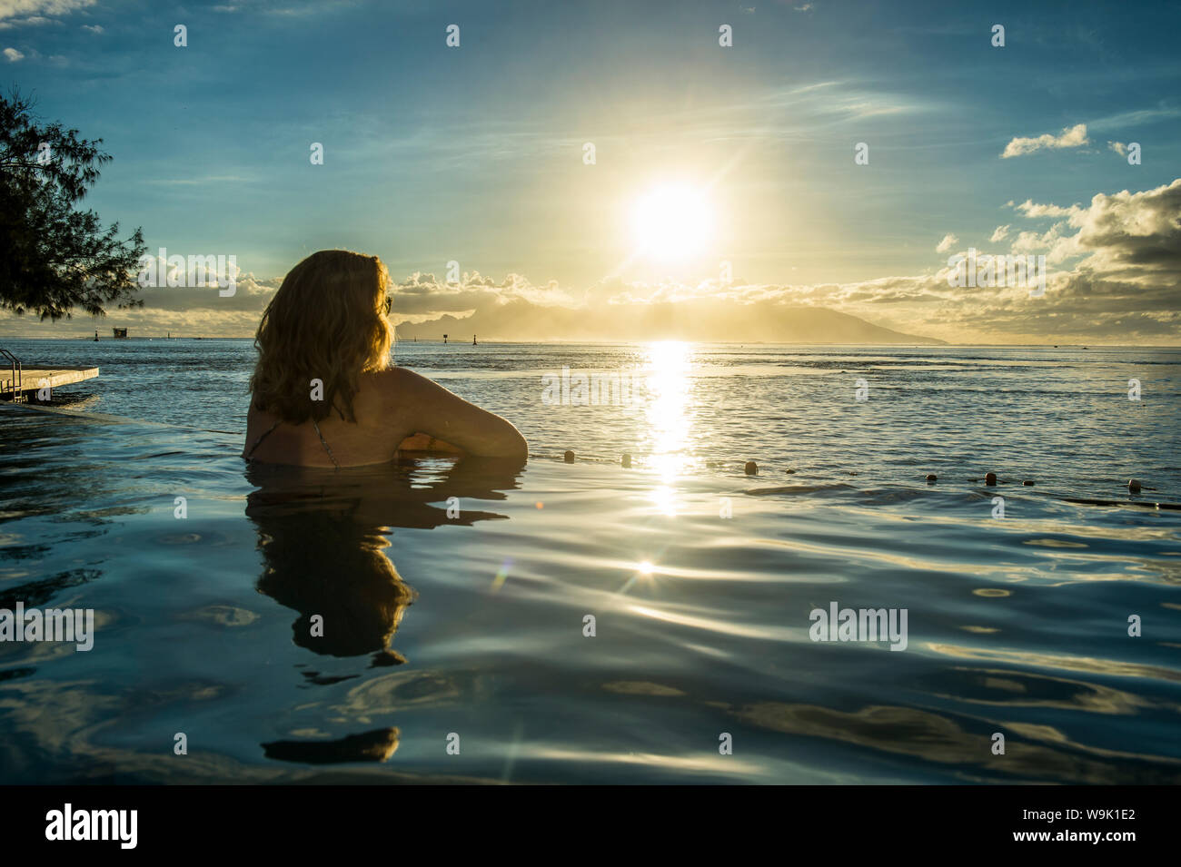 Donna godendo del tramonto in una piscina con Moorea in background, Papeete, Tahiti, Isole della Società, Polinesia francese, Pacific Foto Stock