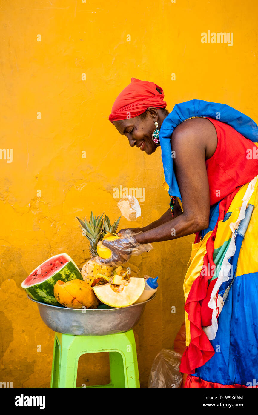 Donna vestito in abiti tradizionali di taglio e la vendita di frutta nella pittoresca città vecchia di Cartagena, Colombia, Sud America Foto Stock
