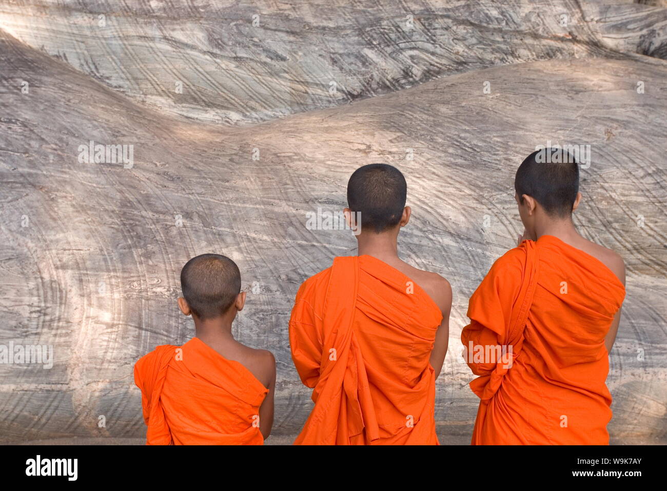 Tre giovani monaci pregando in una rock-cut immagine del Buddha nella Gal Vihara, Polonnaruwa (Polonnaruva), il Sito Patrimonio Mondiale dell'UNESCO, Sri Lanka, Asia Foto Stock