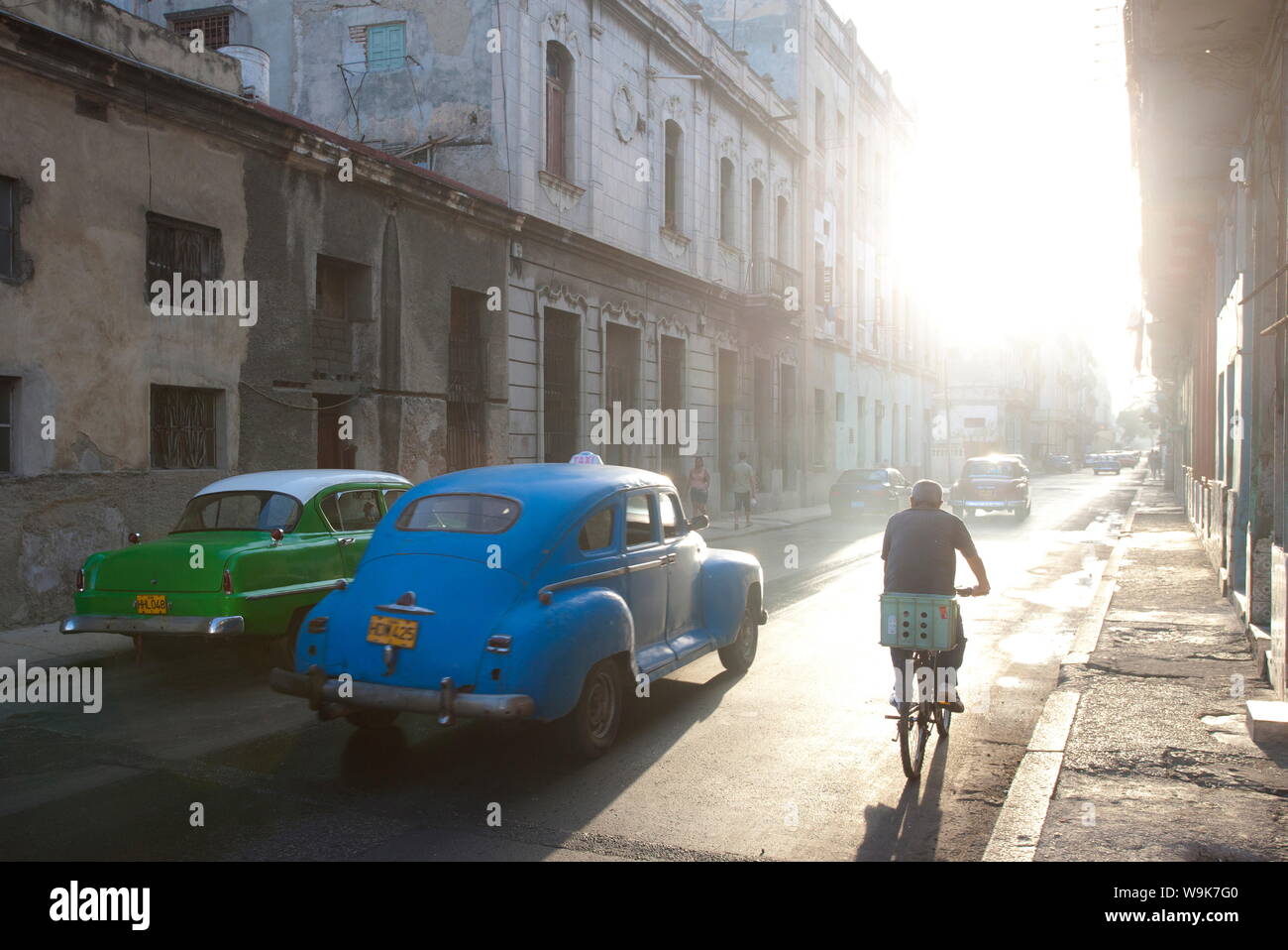 Scena di strada bagnata di prima mattina la luce del sole che mostra vecchie automobili americane e ciclisti, Havana, Cuba, West Indies, America Centrale Foto Stock