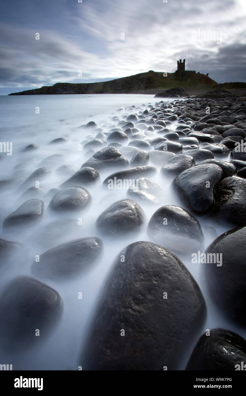 Una lunga esposizione a registrare il movimento in mare, spiaggia di Embleton Bay, Dunstanburgh Castle in distanza, di Embleton Bay, Northumberland, Regno Unito Foto Stock