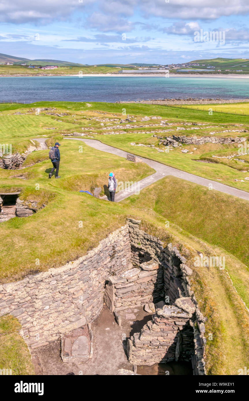 I turisti che visitano una timoneria presso il sito di scavo di Jarlshof vicino Sumburgh Head nel sud del continente, Shetland. West Voe di Sumburgh in background. Foto Stock