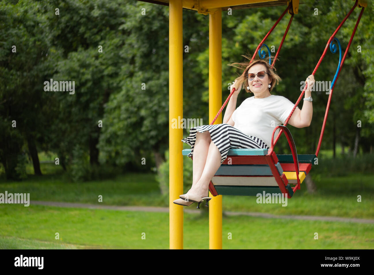 Senior donna matura godendo di pensionamento sensazione di vita felice e sano divertimento basculante in un altalena nel parco in una soleggiata giornata splendida. Foto Stock