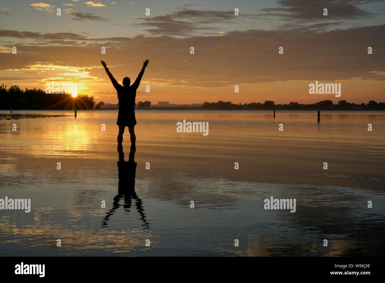 Sunrise silhouette di un uomo in piedi in acqua poco profonda e stretching o praticare chigong movimenti, Boyd il lago del Parco statale nel nord del Colorado Foto Stock