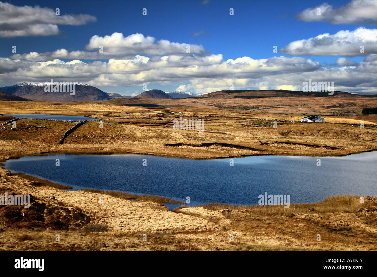 Bellissimo paesaggio irlandese che si affaccia su un lago blu, montagne innevate e nuvole bianche soffici sopra di loro Foto Stock
