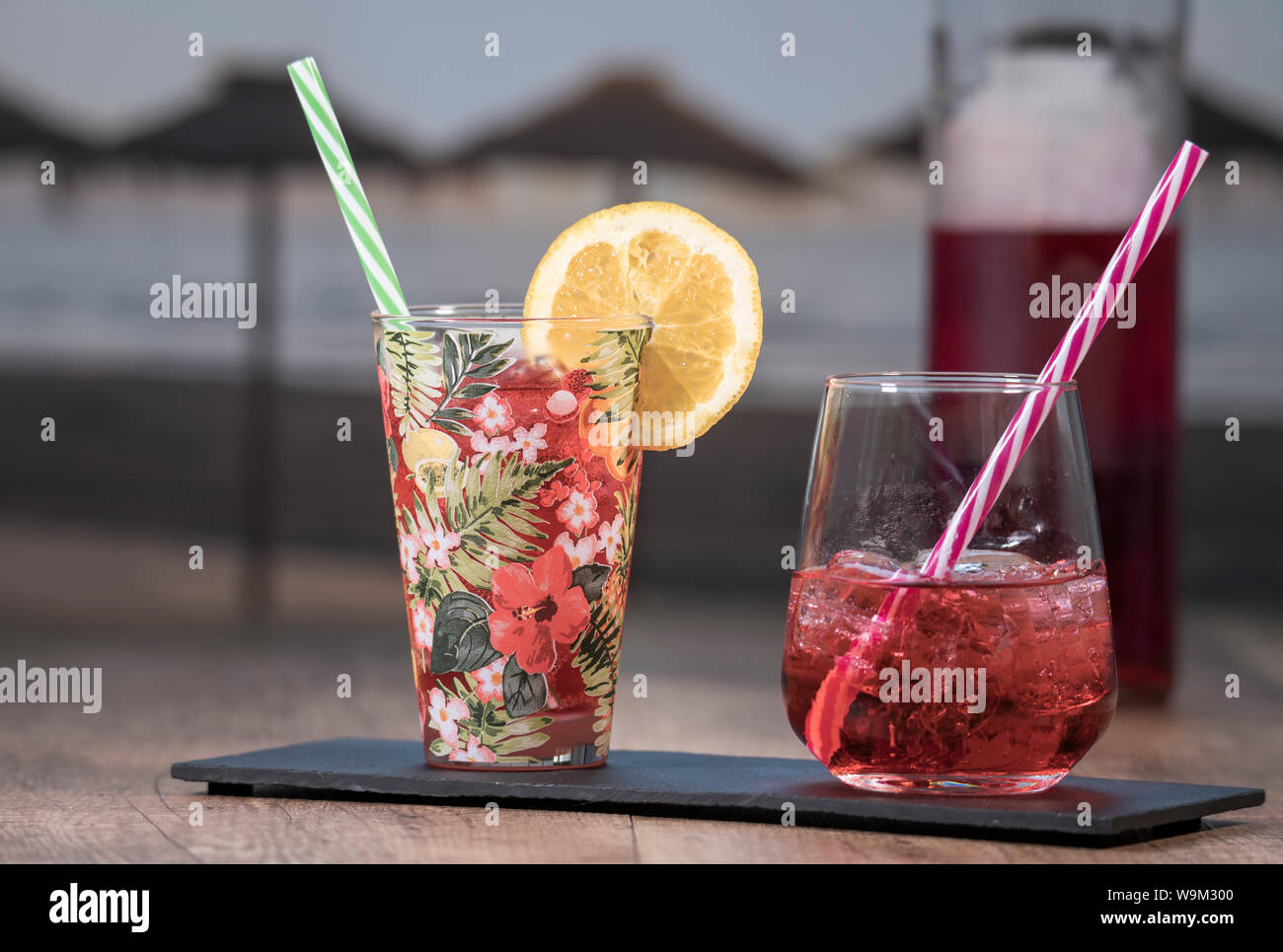 Dettaglio foto di un succo tropicale accanto a un rosso cocktail serviti in un robusto vetro su una pietra nera compressa con una bottiglia in background al di fuori della messa a fuoco. Foto Stock