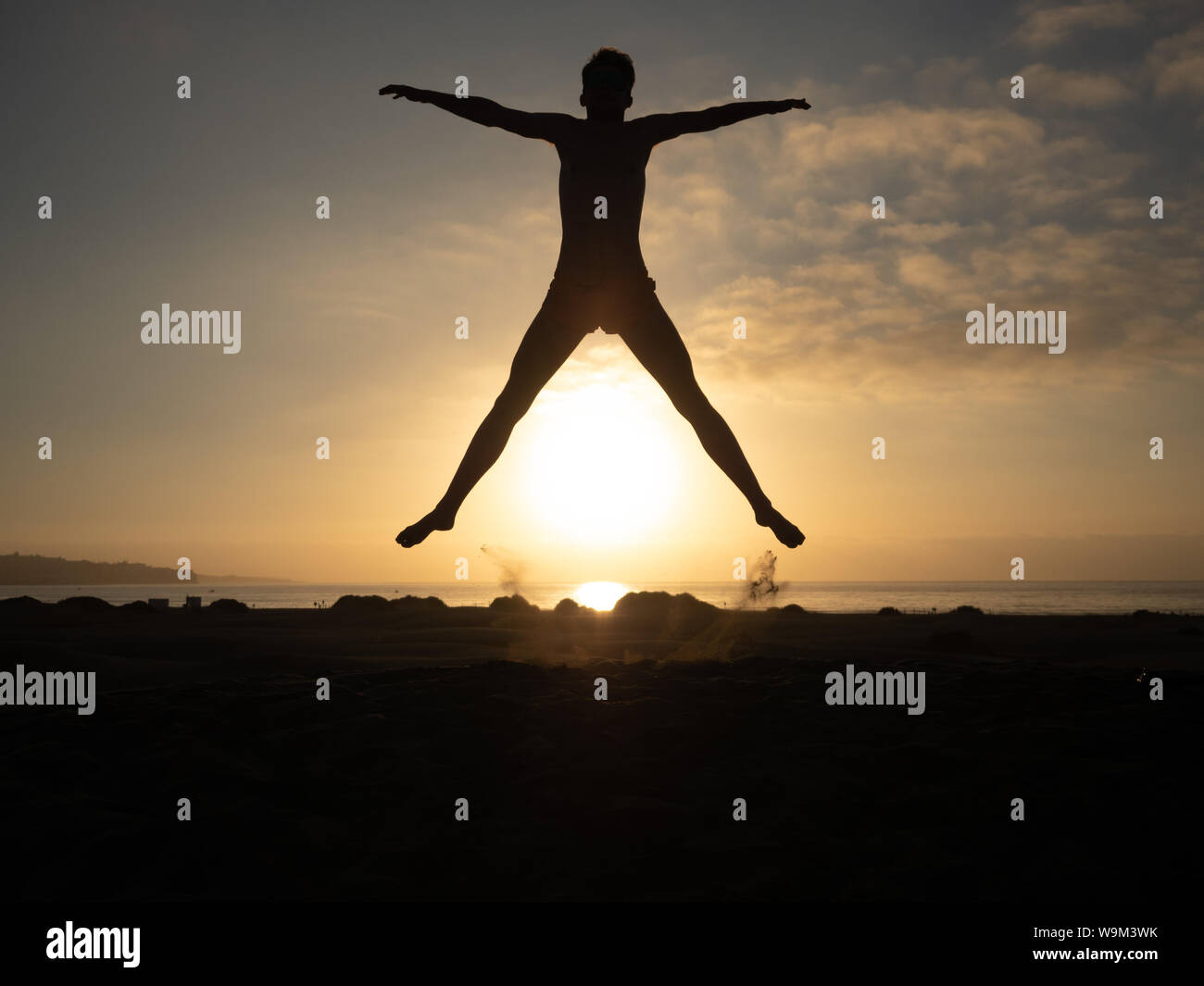 Maschio di salto sulla spiaggia stagliano contro il sorgere del sole. Spiaggia di Maspalomas, Gran Canaria Foto Stock