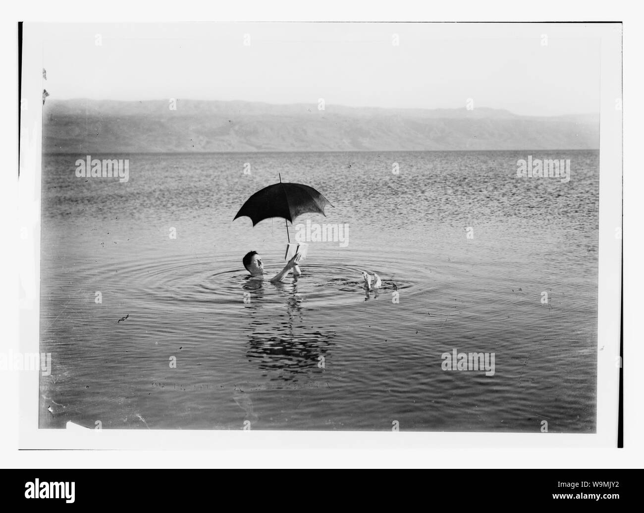 Intorno al Mar Morto. L'uomo flottante con libro e ombrello nelle sue mani Foto Stock
