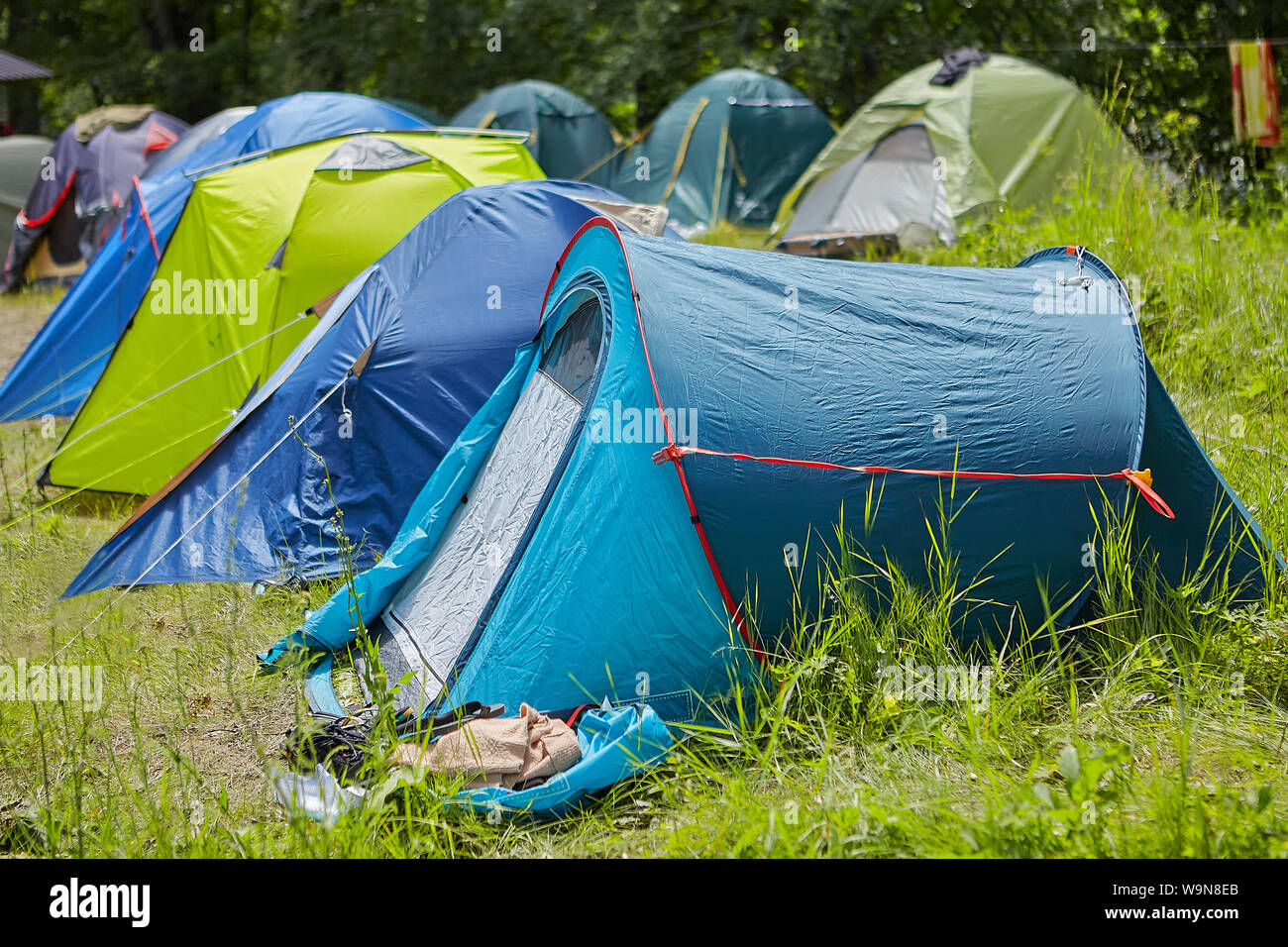 Camping backpackers in una radura del bosco su una soleggiata giornata estiva, un sacco di moderni multi-tende colorate sono impostate sull'erba uno vicino all'altro. Foto Stock