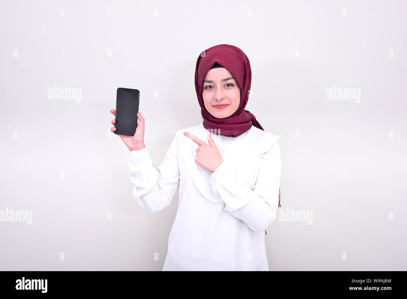 Donna musulmana sorridente e lei sta puntando sullo smartphone, hijab ragazzina musulmana in piedi su sfondo bianco Foto Stock