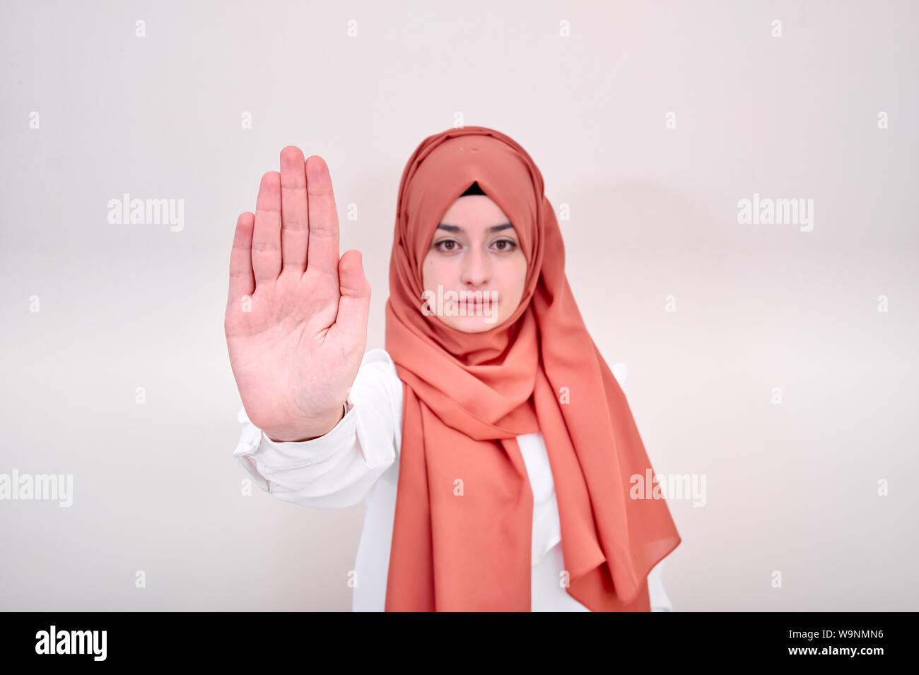 Infelice giovane donna musulmana in piedi con la mano tesa che mostra stop gesto isolato su sfondo bianco Foto Stock