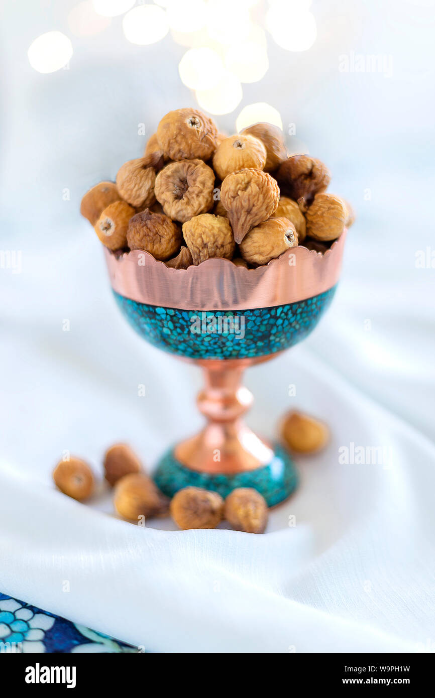 Una ciotola di fichi secchi esposta in un elegante piatto turchese e di rame, che sottolinea l'estetica culturale persiana Foto Stock