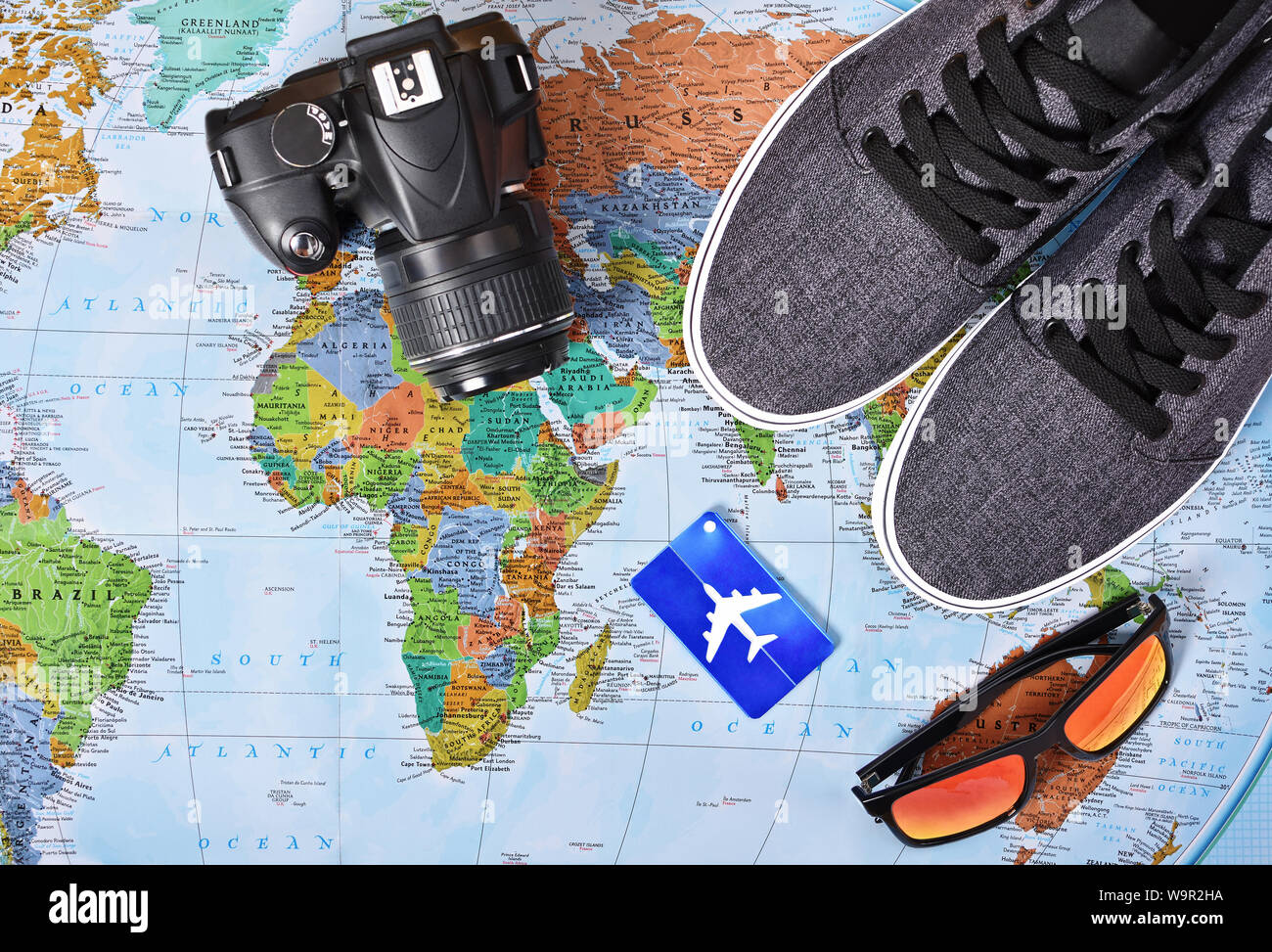 Vista superiore della fotocamera, aeroplano etichetta bagaglio, occhiali da sole e scarpe da ginnastica su una mappa del mondo. Questi sono i miei Travel Essentials per un viaggio intorno al mondo o Foto Stock