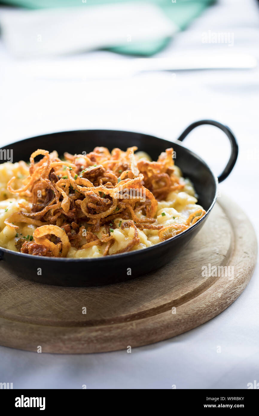 Chiusura del tradizionale formaggio alpino Spätzle in una padella di ferro servita su una tavola di legno Foto Stock