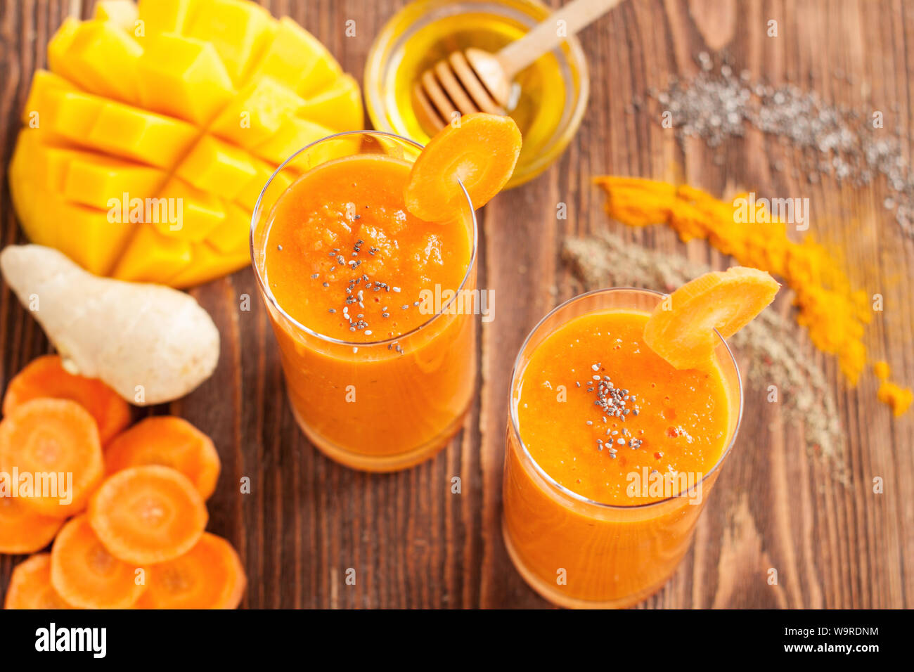 Smoothie con carota, curcuma, mango, zenzero, miele, chia seedss e spezie su tavola in legno rustico Foto Stock