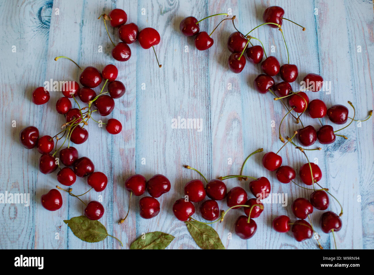 Telaio della red ciliegie mature con foglie verdi su sfondo azzurro, lo spazio per il testo, il concetto di naturale fresco cibo vegetariano Foto Stock