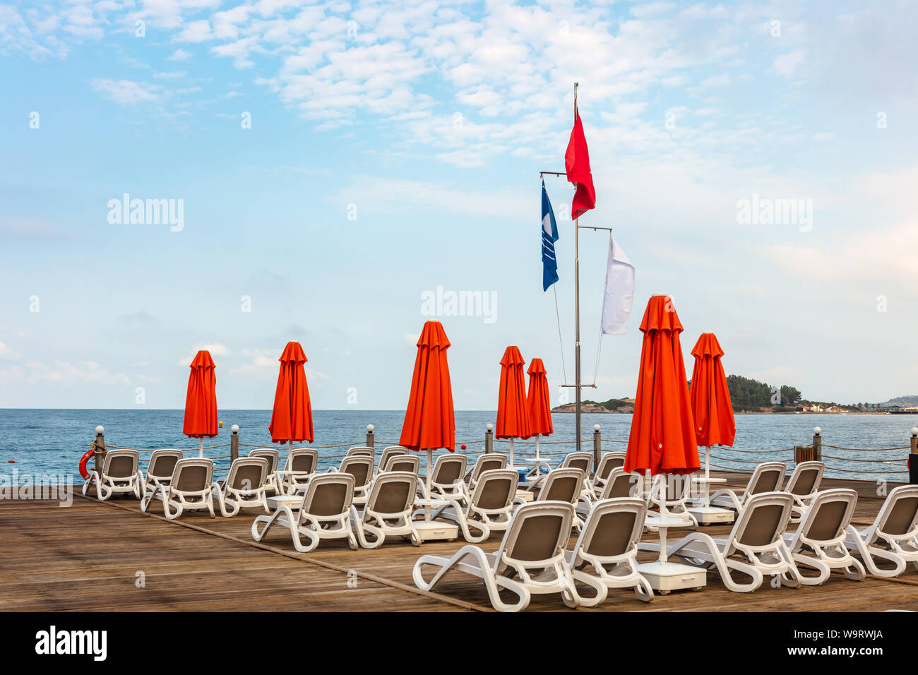 Righe bianche di lettini con ombrellone rosso su un molo in legno in mare. Foto Stock