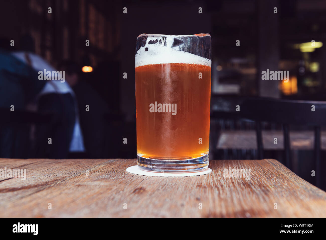 Un bicchiere di birra con la schiuma su un tavolo di legno. Un sorso di marrone rinfrescante drink nel bar. La solitudine. Foto Stock