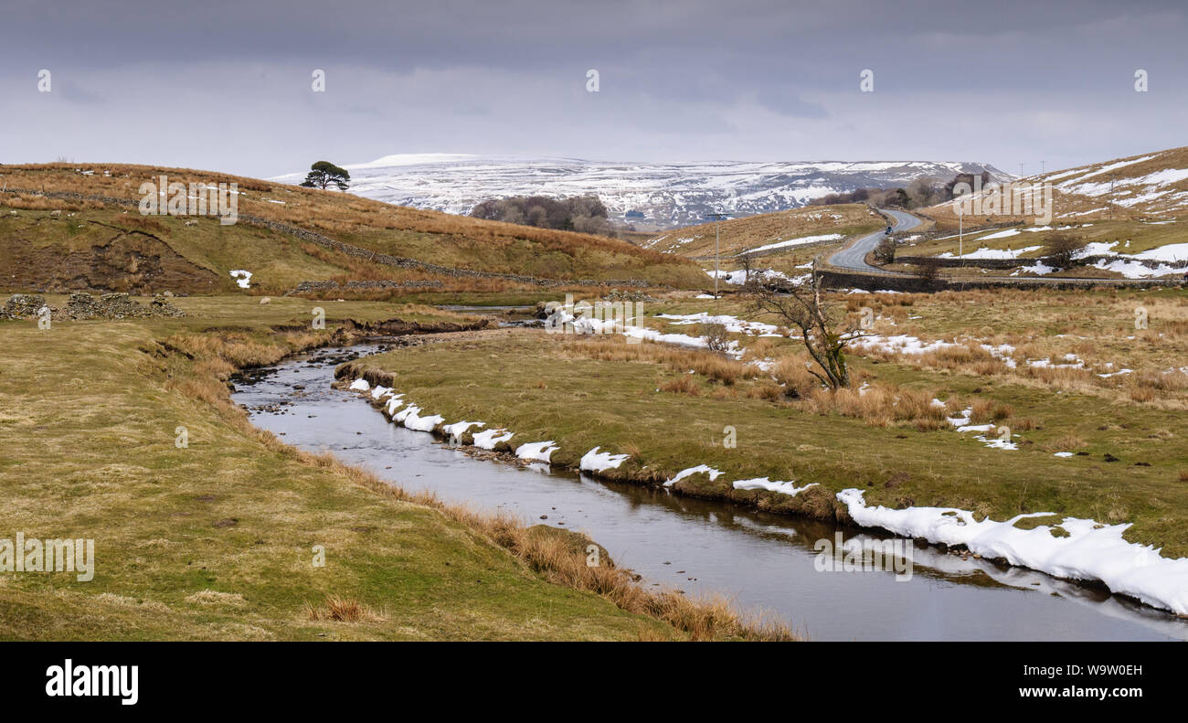 Macchie di neve invernale giacciono su pascolo accanto Widdale Beck fiume nella valle Widdale vicino Hawes in Inghilterra del Yorkshire Dales. Foto Stock