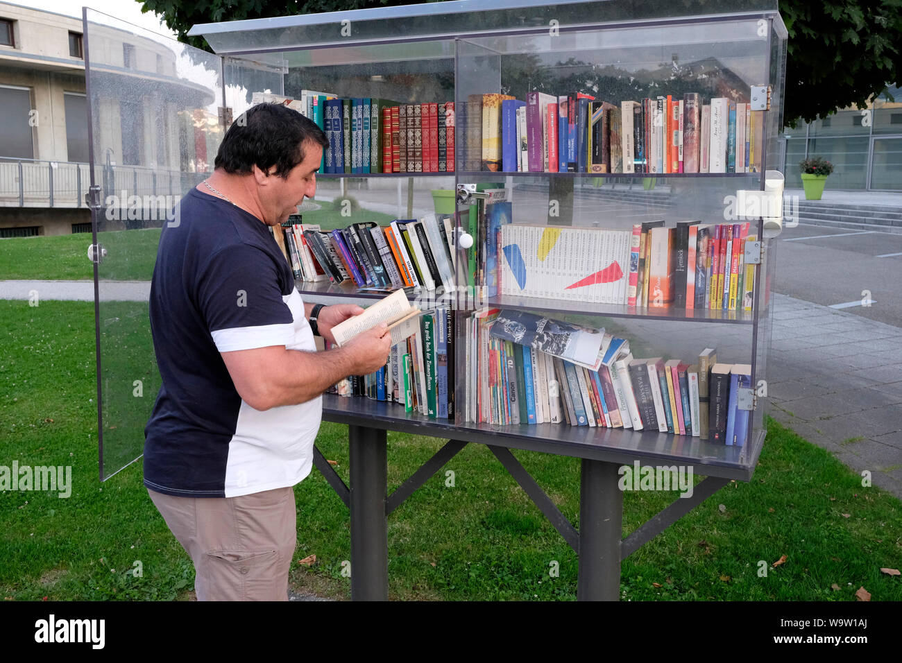 Un uomo libri di esplorazione in un libero piccola biblioteca, Huningue, Francia Foto Stock