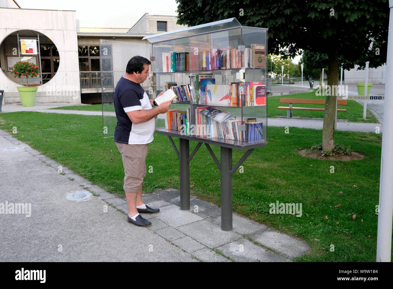 Un uomo navigando in un libro in un libero piccola biblioteca, Huningue, Francia Foto Stock