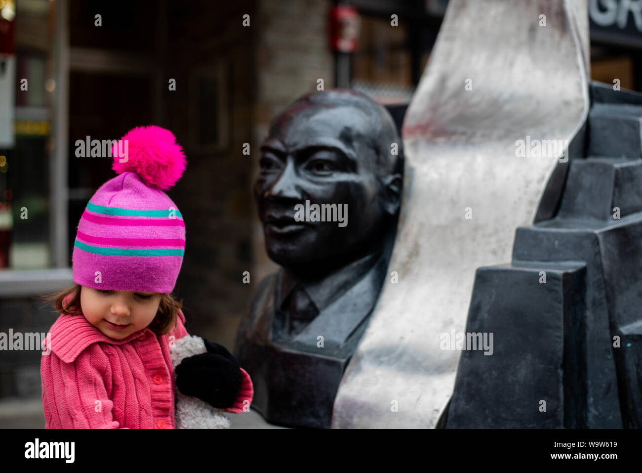 Un bambino ragazza sorge accanto alla statua di Martin Luther King Jr., in Ithaca NY nel mezzo dell'inverno. Foto Stock