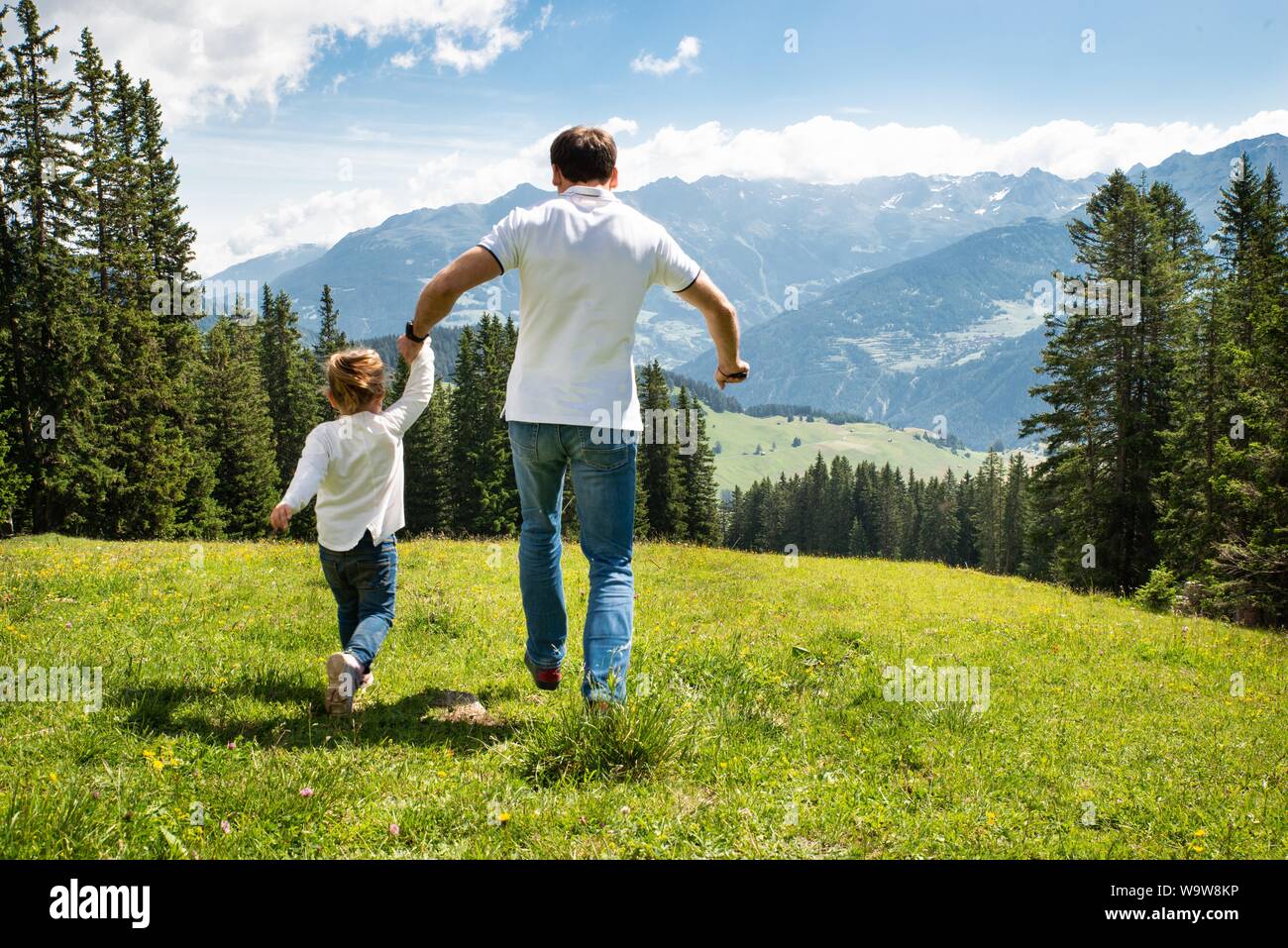 Padre e figlia tenendo le mani in esecuzione sul campo in montagna Foto Stock