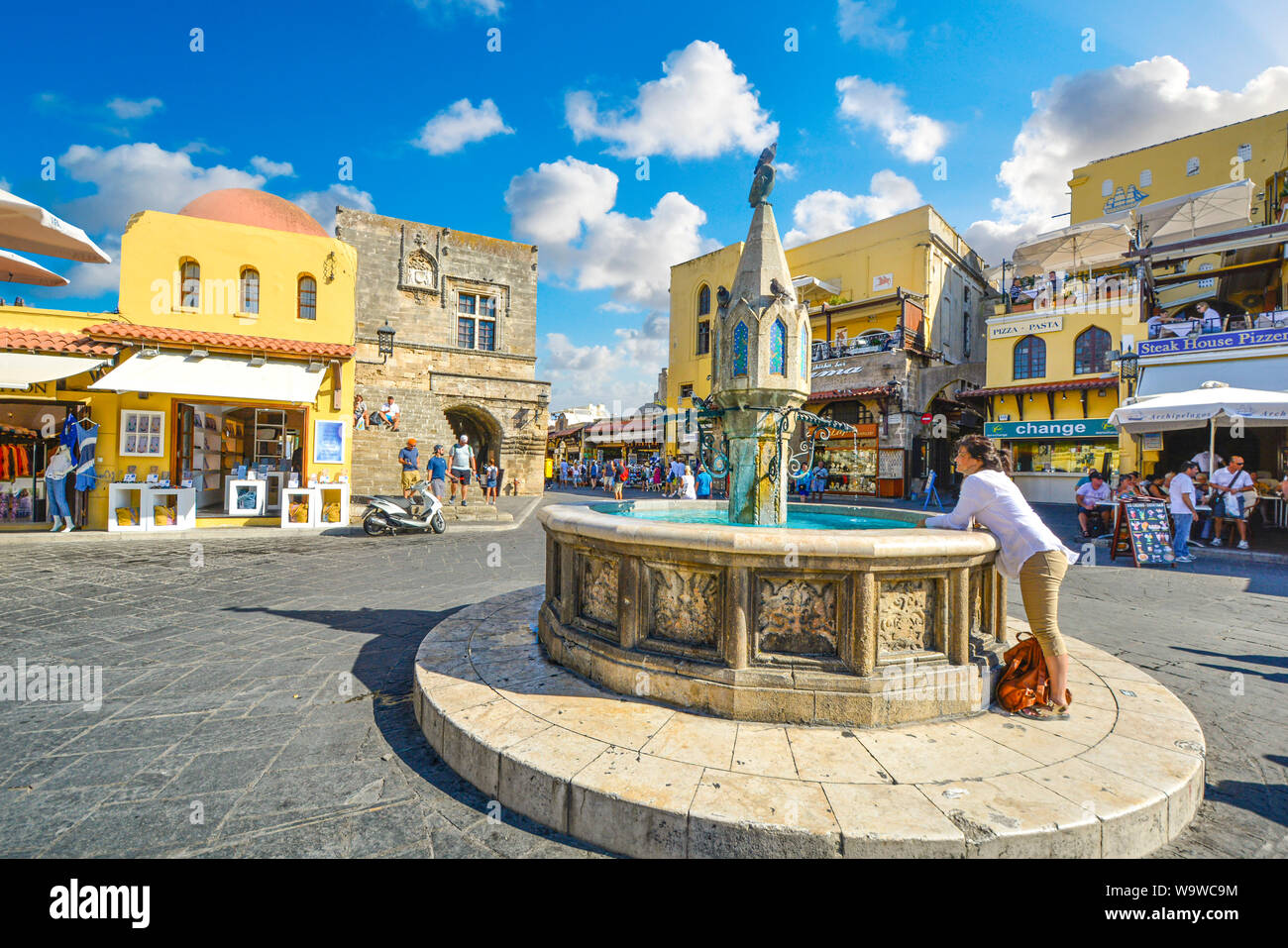 Una donna si rilassa presso la fontana nella Città Vecchia di Ippocrate quadrato in un giorno di estate sull'isola Mediterranea di Rodi, Grecia Foto Stock