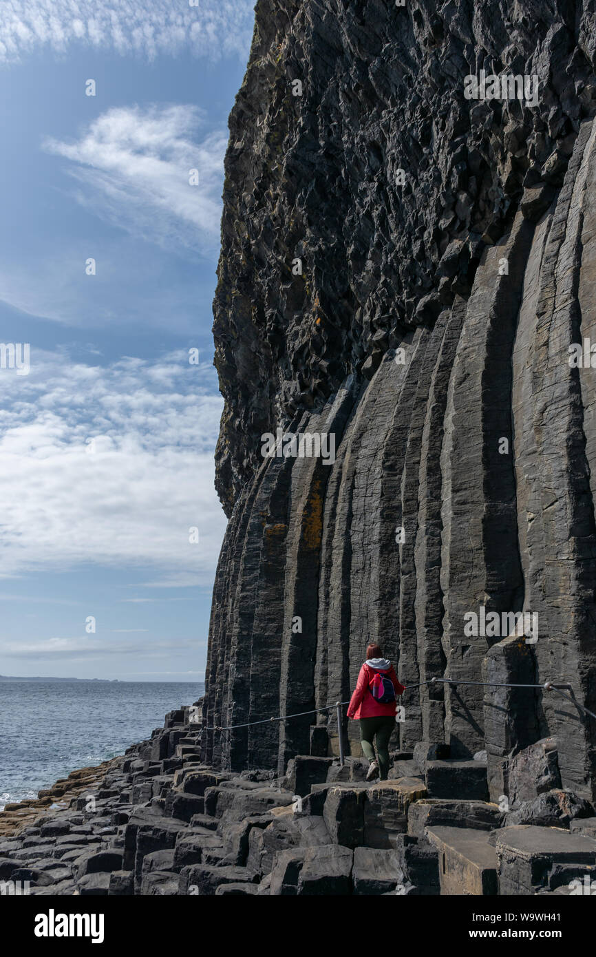 Donna (età 40-50) cammina al fianco della scogliera di Finghal's Cave, Staffa Isola, Argyll and Bute, Scozia durante la breve pausa nel mese di agosto Foto Stock