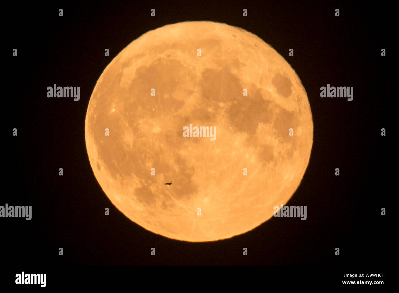 Londra, Regno Unito. Il 15 agosto 2019. Un aereo passa di fronte al Full Moon Rising su Wembley, a nord ovest di Londra. Il mese di agosto la luna piena è spesso chiamato lo storione Luna, secondo il vecchio contadino di almanacco, perché lo storione (un tipo di pesce) sono più facilmente catturata nel mese di agosto e i primi di settembre. Credito: Stephen Chung / Alamy Live News Foto Stock