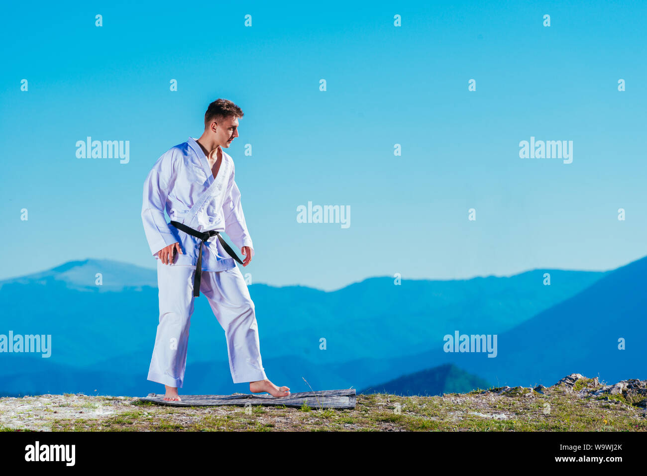 Montare il karate atleta calci una tazza riempita whit fluor causando un grande splash indossando un kimono bianco sulla cima di una montagna in una giornata di sole. Foto Stock