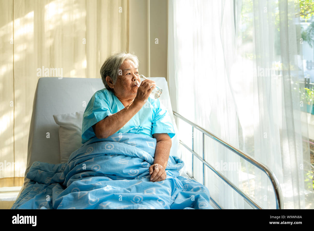 Asian anziani donna seduta e tenendo un bicchiere di acqua nel letto di ospedale. Foto Stock