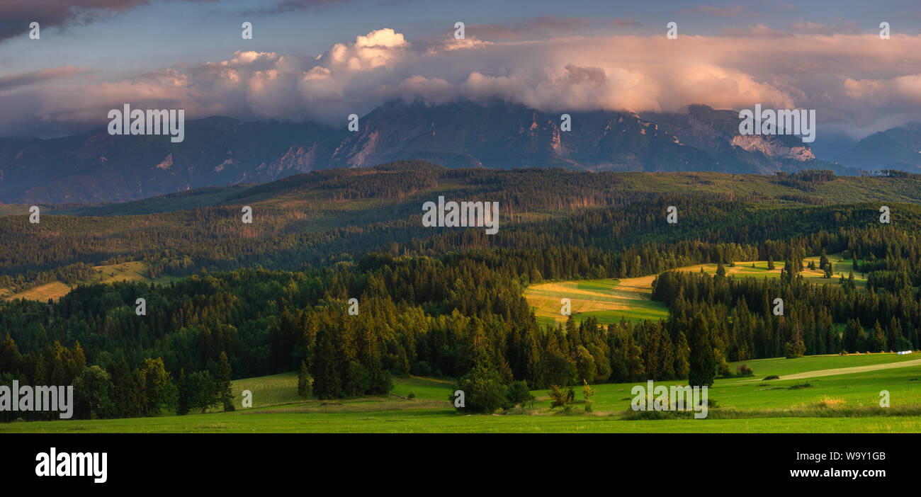 Panorama dei Monti Tatra. Picchi di montagna svettante su verdi colline erbose. Al di sopra dei picchi, bella nuvole temporalesche illuminato dall'impostazione s Foto Stock