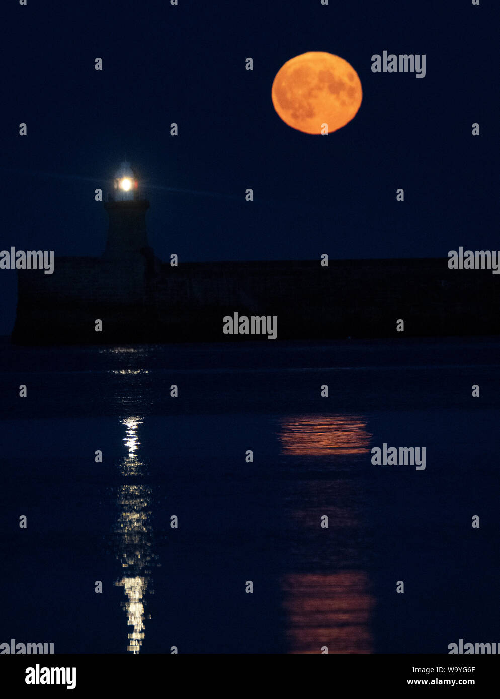 Una luna piena, noto come una luna di storione, sorge su South Shields faro nel nord-est dell'Inghilterra. Foto Stock