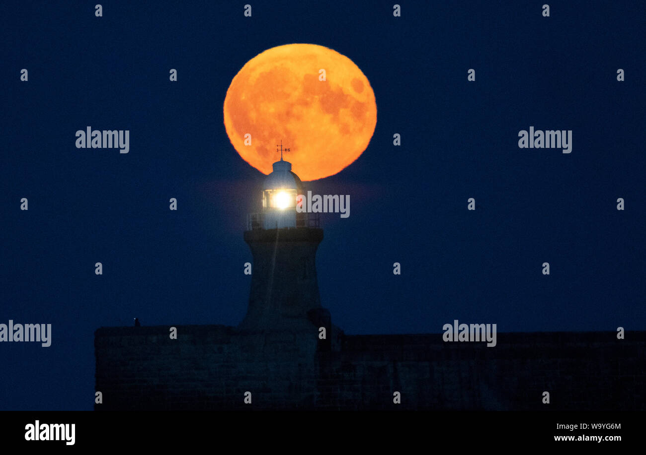 Una luna piena, noto come una luna di storione, sorge su South Shields faro nel nord-est dell'Inghilterra. Foto Stock