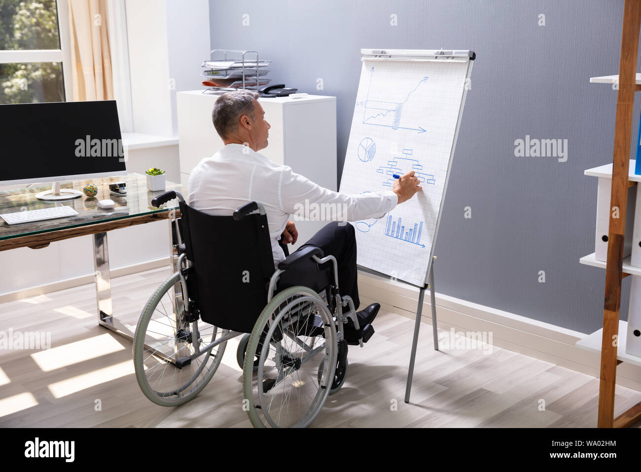 Imprenditore disabile seduto su una sedia a rotelle in ufficio lo schema di disegno sulla lavagna a fogli mobili Foto Stock