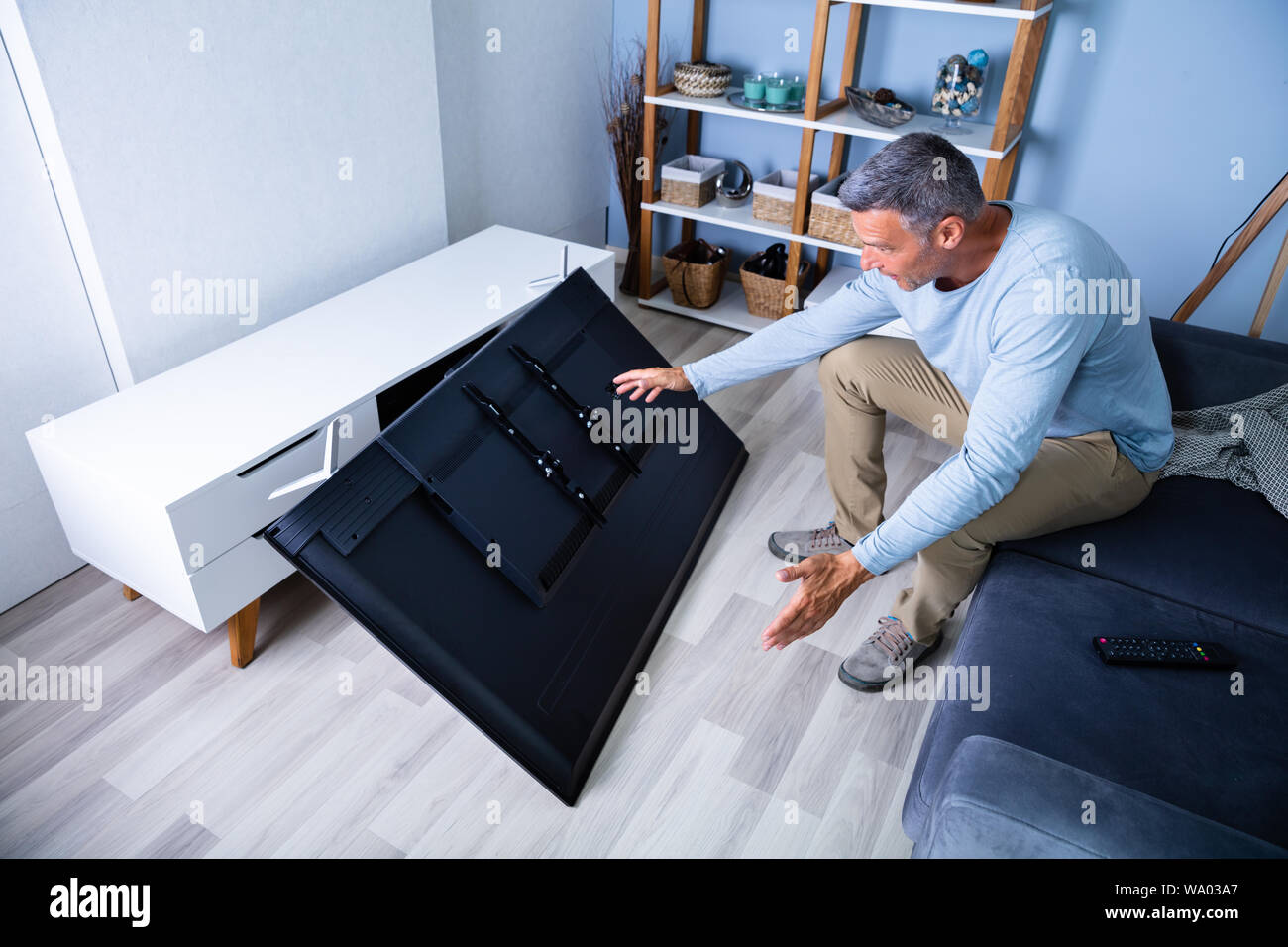 Uomo seduto sul divano davanti caduti televisione con schermo rotto Foto Stock