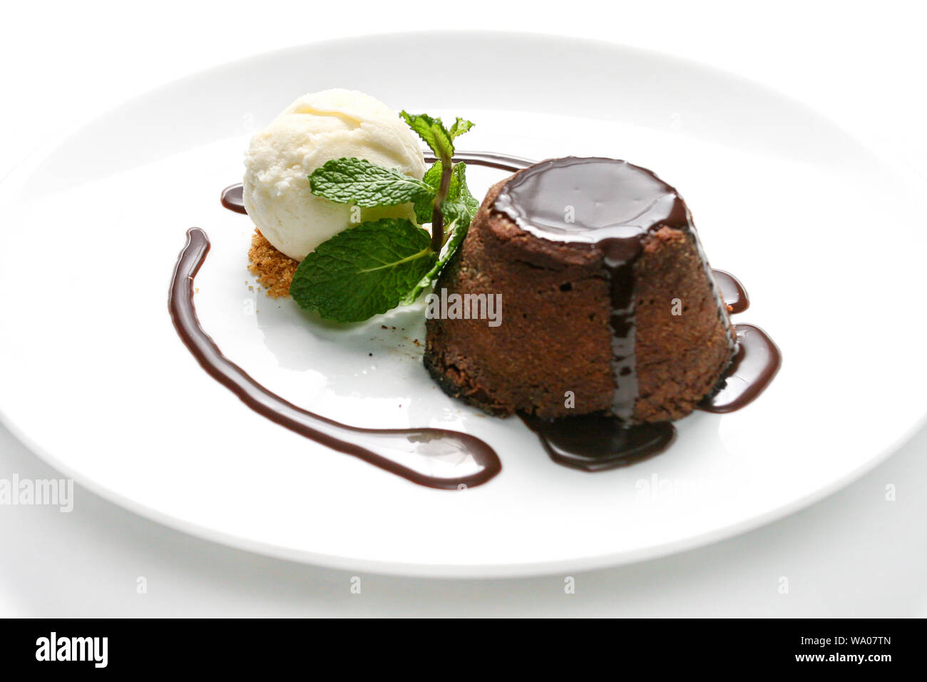 Delizioso 'petit gateau' torta al cioccolato con sciroppo di cacao, gelato alla vaniglia e foglia di menta servito sulla piastra bianca con sfondo bianco. Foto Stock