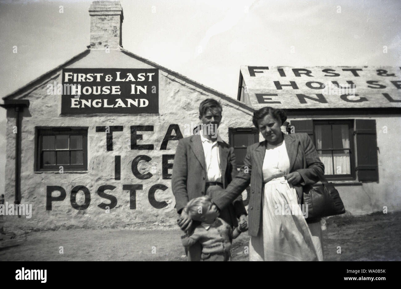 1950, storico, una madre con i suoi due figli al di fuori della " prima e ultima casa in Inghilterra', un vecchio cottage che funzioni come una sala da tè ed un piccolo negozio vendita di gelati e negozio di souvenir presso la costa a Lands End, Cornwall, Inghilterra, Regno Unito. Foto Stock