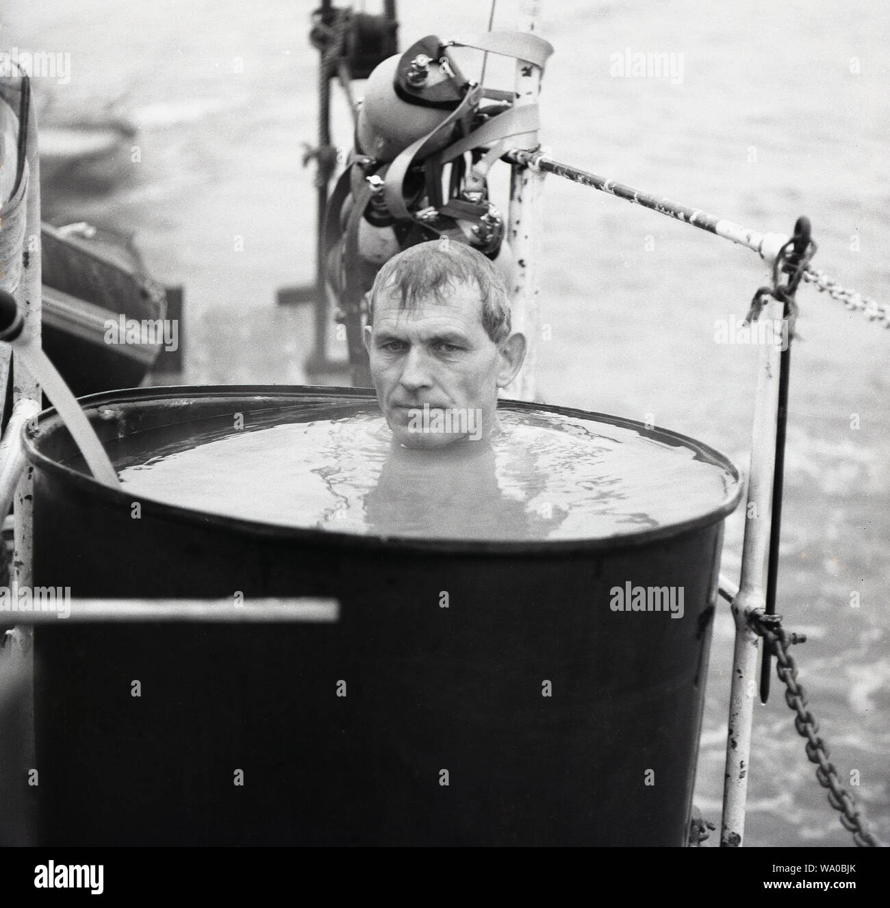 Degli anni Cinquanta, storico, un shipman seduta in una vasca riempita con acqua fuori sul ponte di una nave, Foto Stock