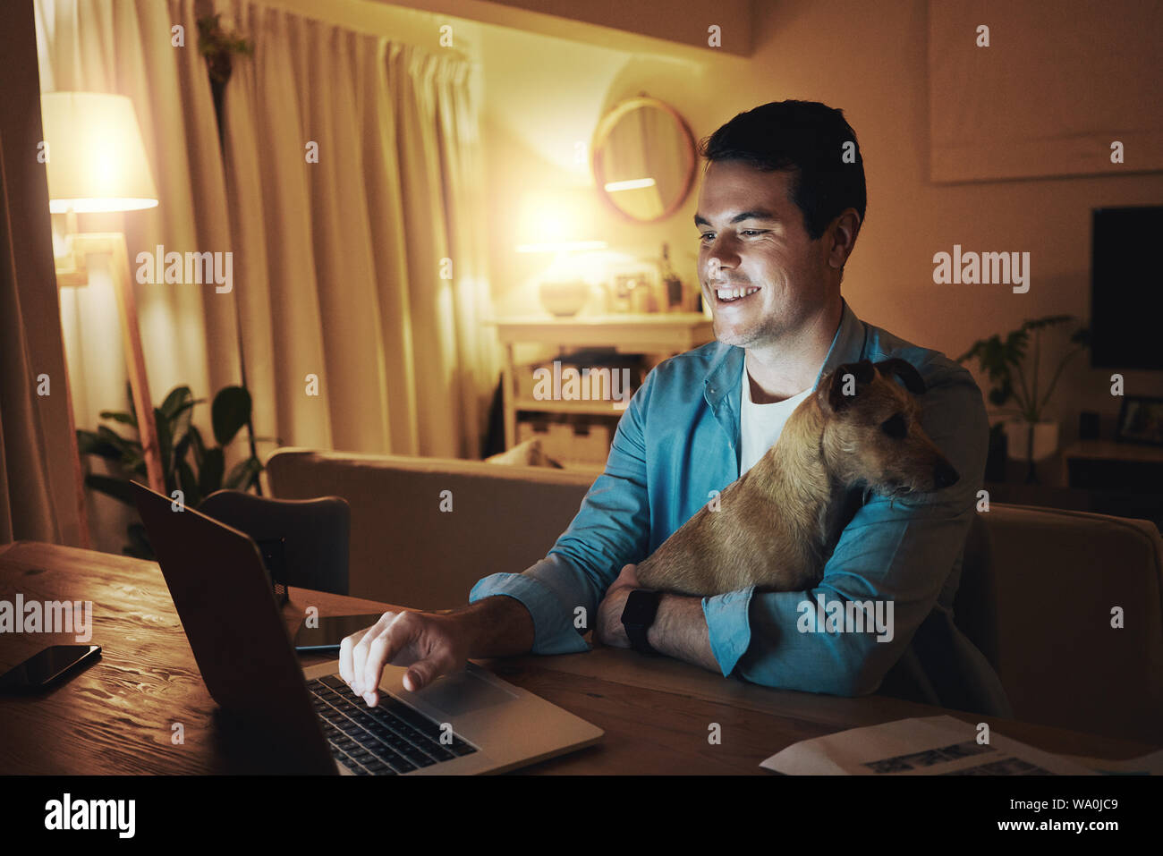 Felice l'uomo con il suo cane utilizzando portatile a casa Foto Stock