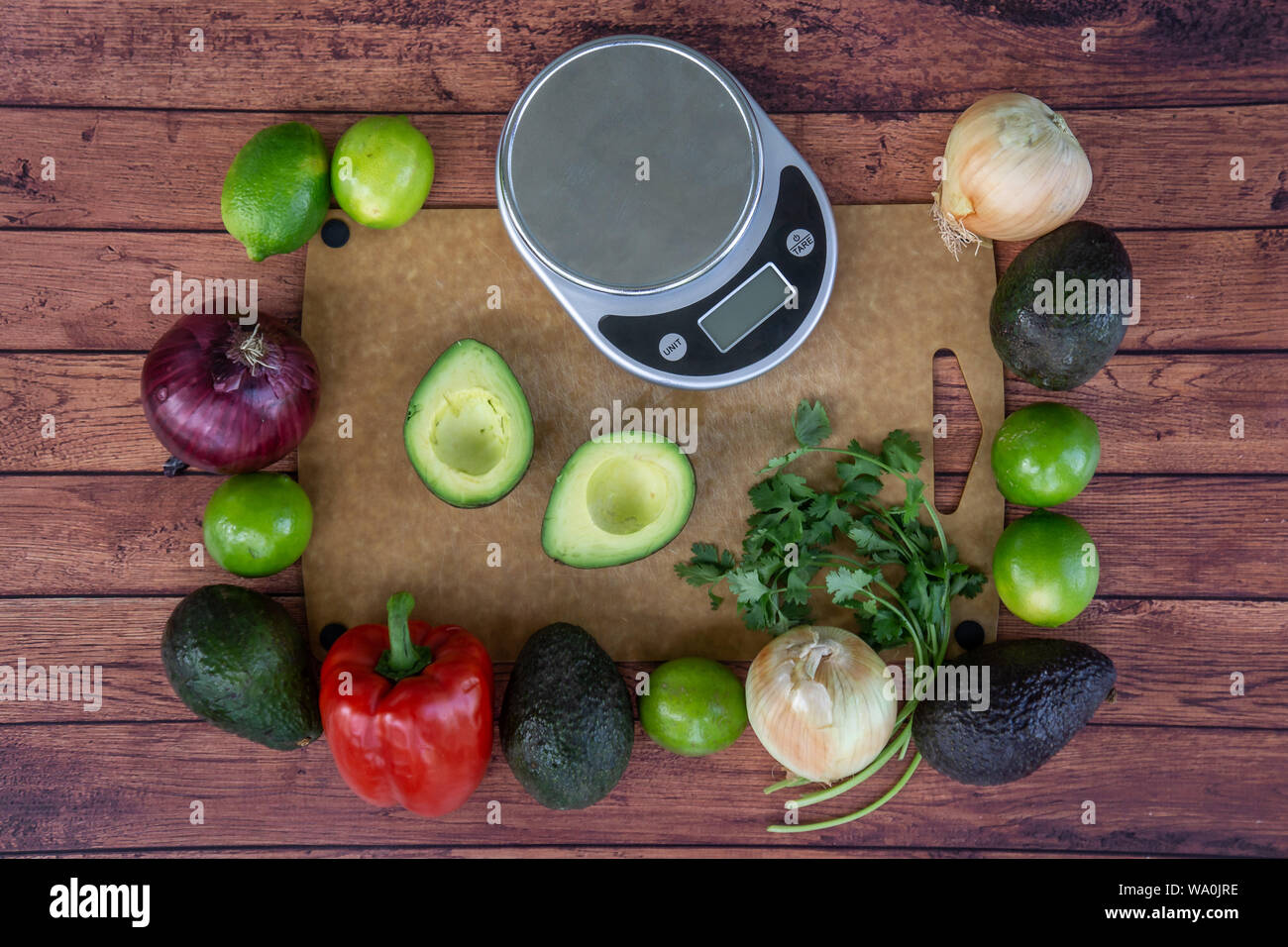 Top vista aerea del guacamole fresco ingredienti con un peso scala. Avocado tagliati a metà e coriandolo fresco, il peperone rosso, verde lime e le cipolle. H Foto Stock