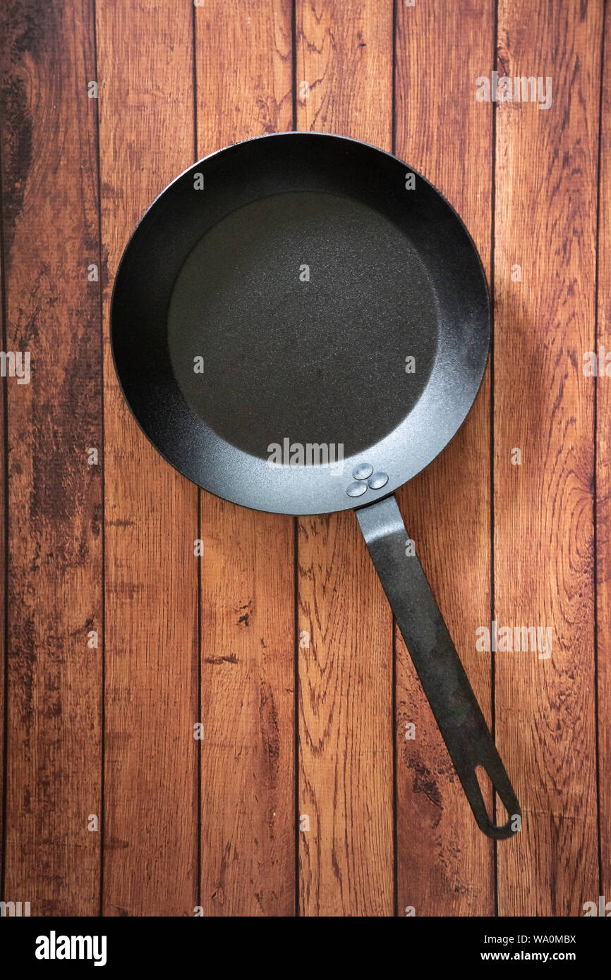 Isolare in acciaio al carbonio skillet pan su un sfondo di legno - tetto vista dall'alto del piatto concetto laici. Professional grade pentole arnese apparecchiature utilizzate in Foto Stock