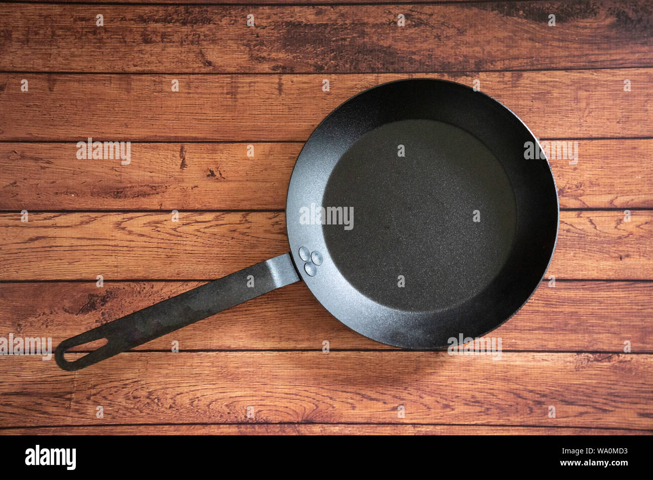 Isolare in acciaio al carbonio skillet pan su un sfondo di legno - tetto vista dall'alto del piatto concetto laici. Professional grade pentole arnese apparecchiature utilizzate in Foto Stock