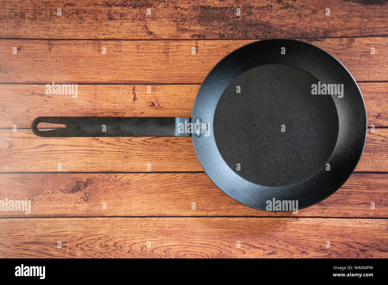 Isolare in acciaio al carbonio skillet pan su un sfondo di legno - tetto vista dall'alto del piatto concetto laici. Professional grade pentole arnese apparecchiature utilizzate in Foto Stock