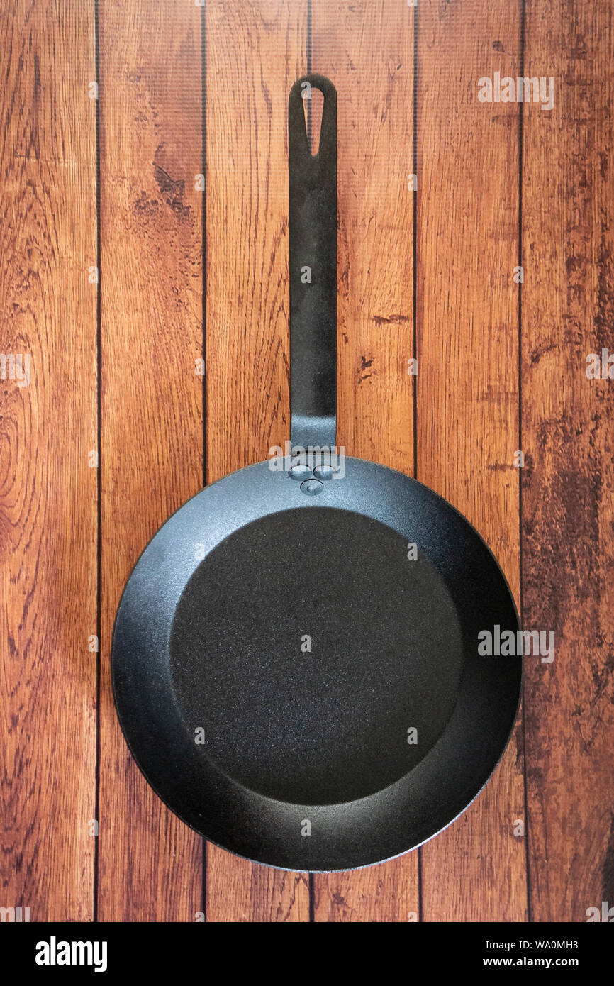 Isolare in acciaio al carbonio skillet pan su un sfondo di legno - tetto vista dall'alto del piatto concetto laici. Professional grade pentole arnese apparecchiature utilizzate in Foto Stock